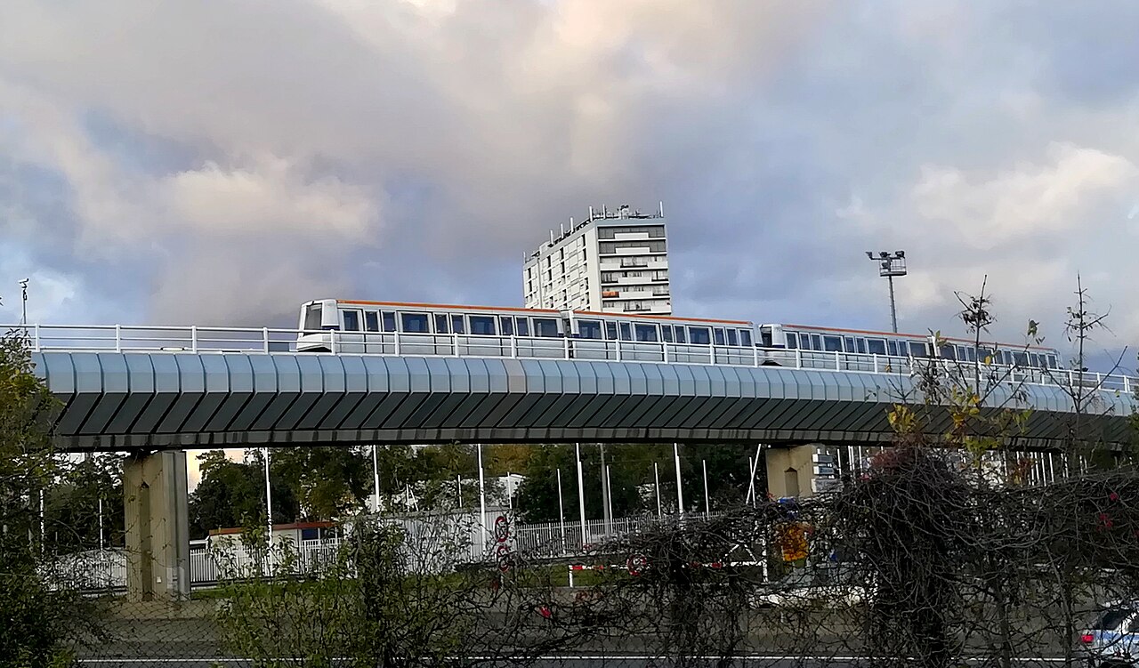 Rame VAL blanche à bandeau orange sur viaduc, métro de Toulouse, immeuble blanc en fond.