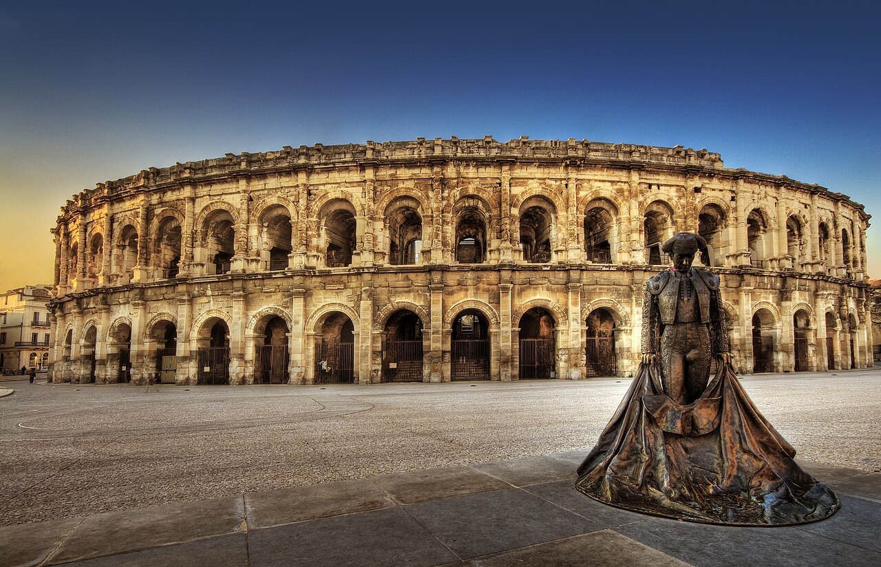 Arènes de Nîmes au soleil rasant, statue de bronze du torero Nimeño II sur la place.