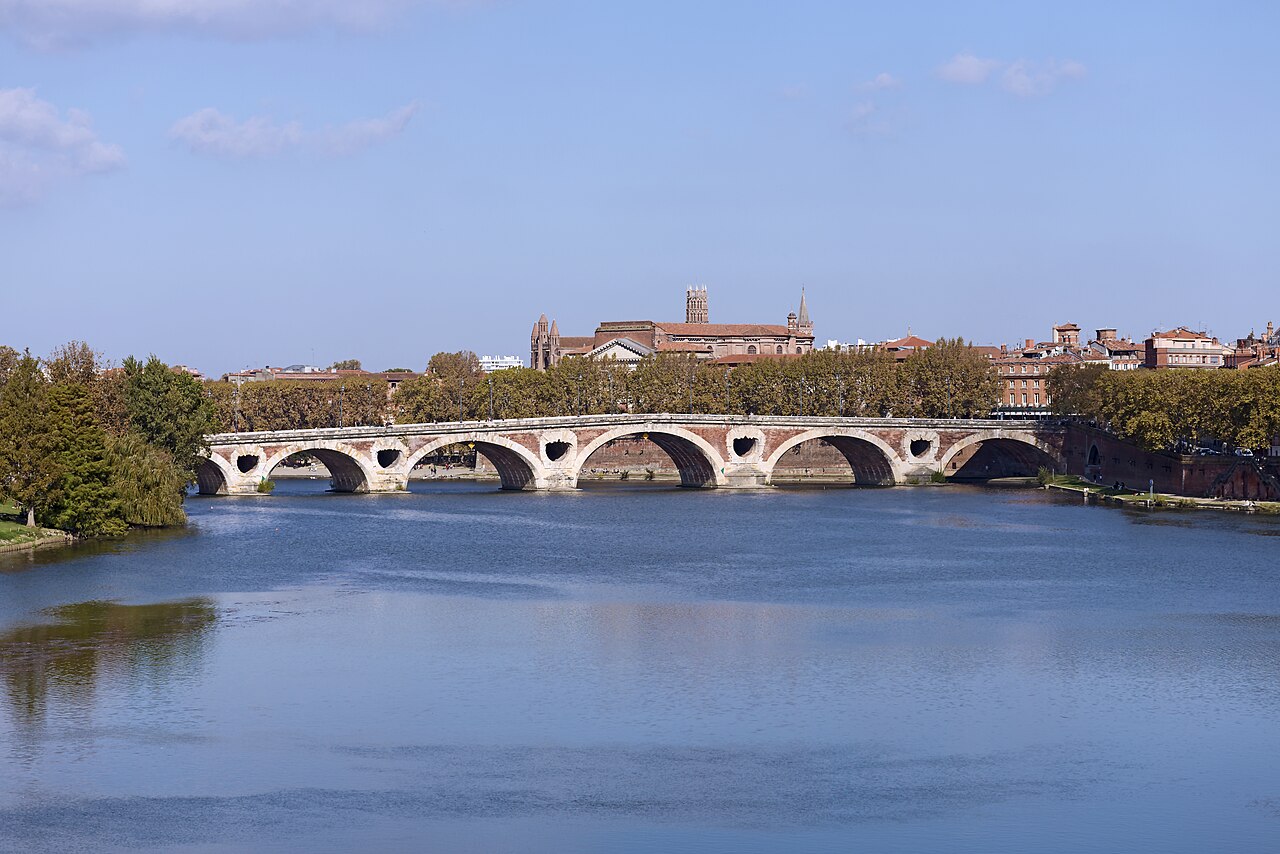 Pont-Neuf de Toulouse, arches de brique et pierre sur la Garonne, toits et clocher en arrière-plan.